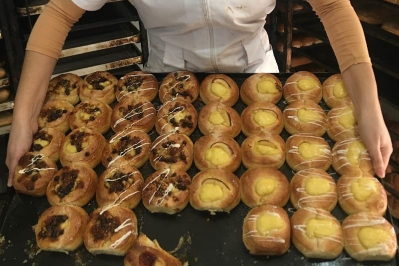 Marina in the bakery in Argentina where she learned to bake, lifting a full tray of pastries straight from the rack