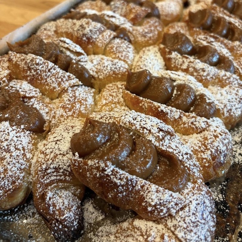 A close crop of dulce de leche medialunas under a heavy dusting of powdered sugar, baked in Richmond, VA
