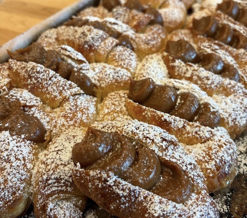 Fresh Argentine dulce de leche medialunas dusted with powdered sugar, on the tray they were baked in, in Richmond, VA