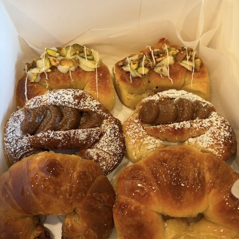 An open white box of assorted medialunas — plain, dulce de leche and pistachio cream — packed for pickup in Richmond, VA