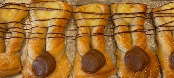 A row of flaky pastries drizzled with chocolate, each topped with a round of chocolate, on the tray they were baked on