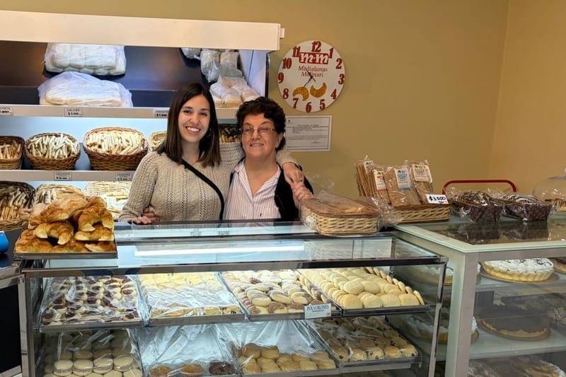 Two women behind the counter of Medialunas Molinari, the family bakery in Argentina the medialuna recipe comes from, a tray of medialunas on the case beside them