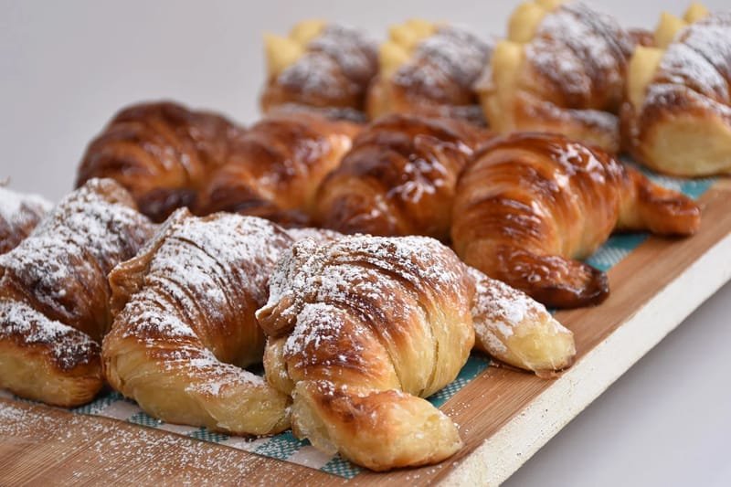 Medialunas dusted with powdered sugar, laid in rows on a wooden board
